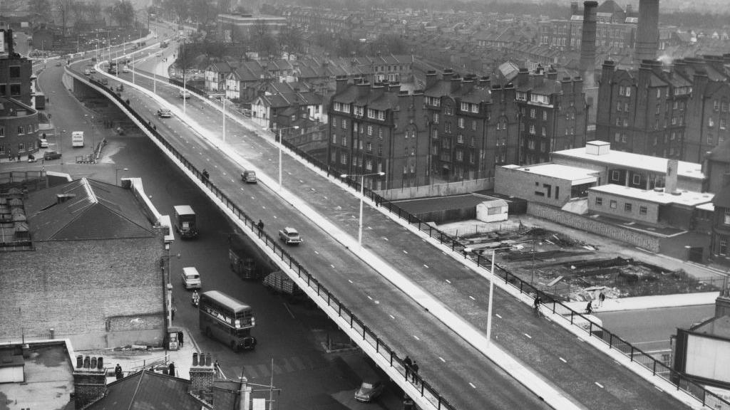 A black and white image of the road system in 1961, featuring older cars and buses. 