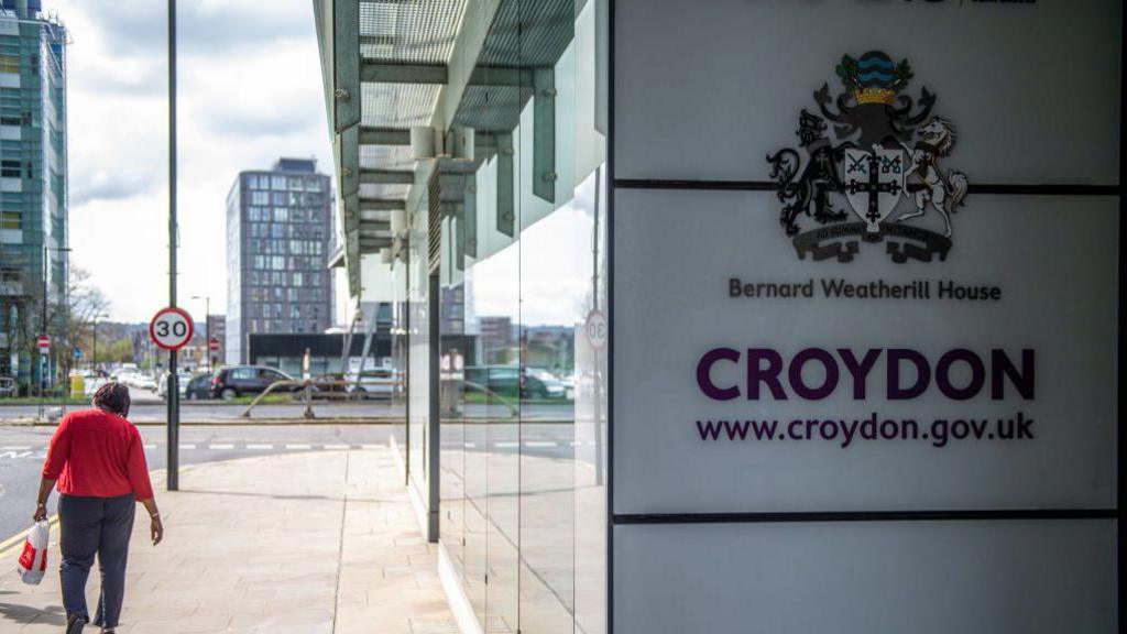 A pedestrian walks past Bernard Weatherill House, home to Croydon Council, with a visible council logo and website on the building exterior.