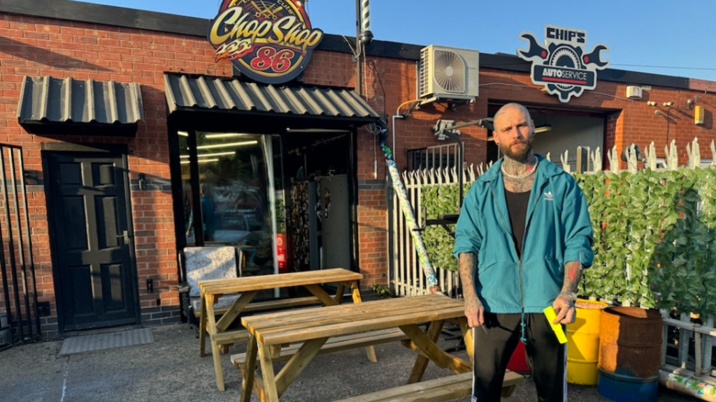 Evan Swift, wearing a green hoodie and black jogging bottoms, is pictured outside his shop. A sign above the building reads Chop Shop 86