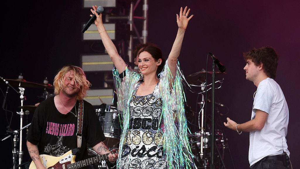 Sophie Ellis-Bextor, dressed in a sparkly, silver dress that says "disco" repeatedly joins Royel Otis with her hands up in the air with a microphone in her right hand.