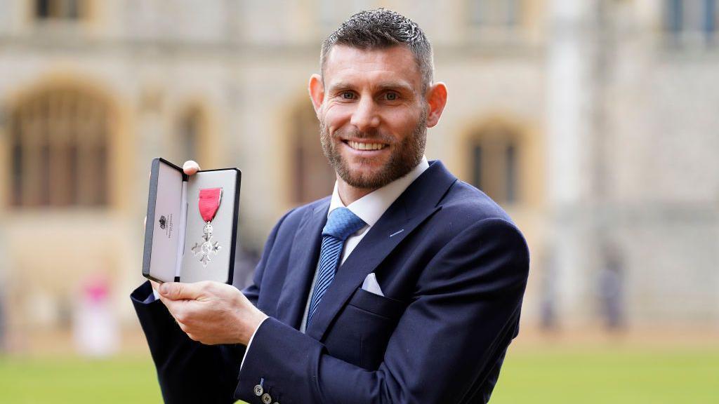James Milner smiling with his MBE award.