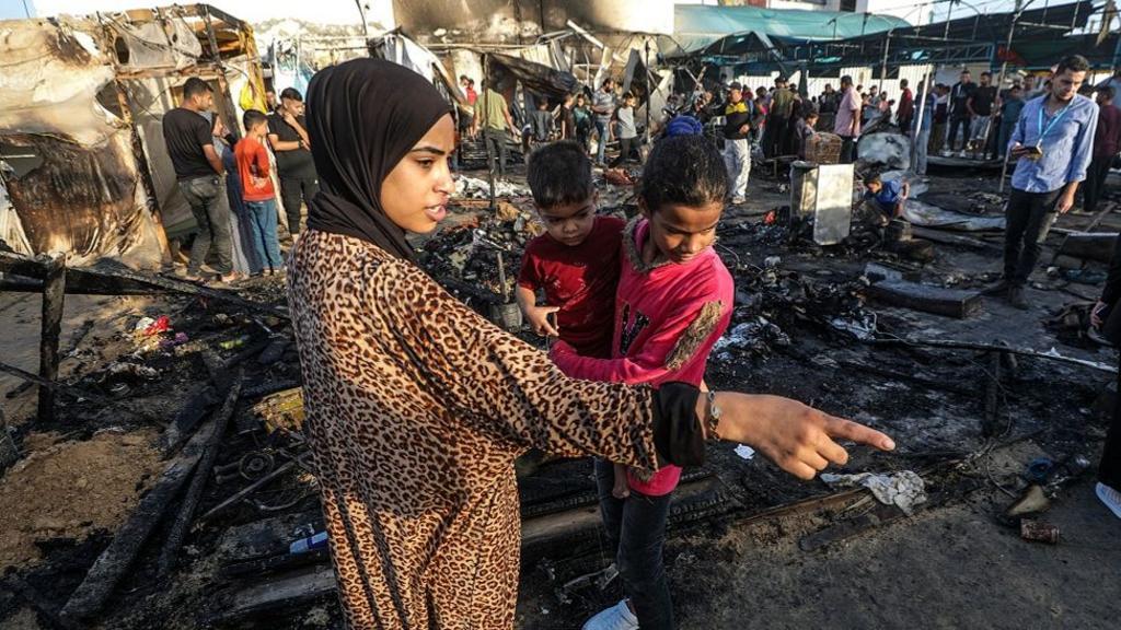 Palestinians survey the damage at a camp for internally displaced people on the premises of al-Aqsa Hospital, after the area was hit by an Israeli air strike