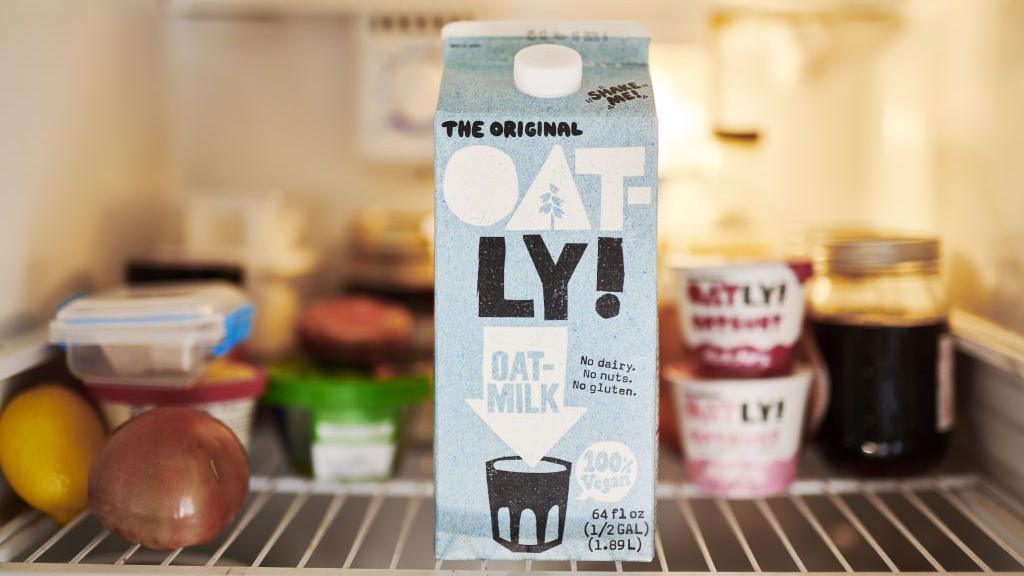 A carton of Oatly plant-based drink displayed alongside a traditional dairy milk bottle, with a symbolic gavel in the foreground representing the court ruling.