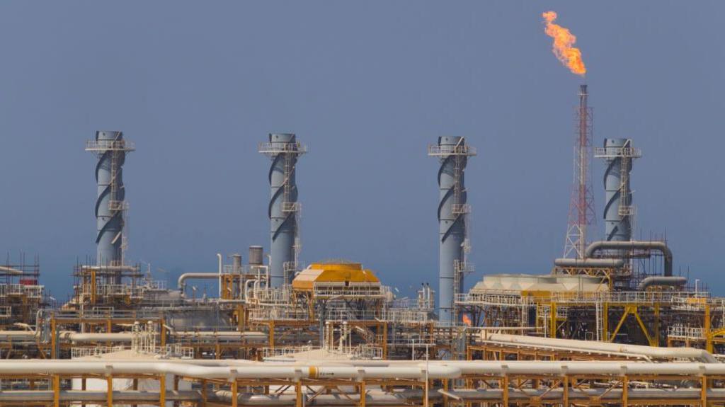 Four chimneys at a gas field are pictured with fire being emitted from a fifth chimney.