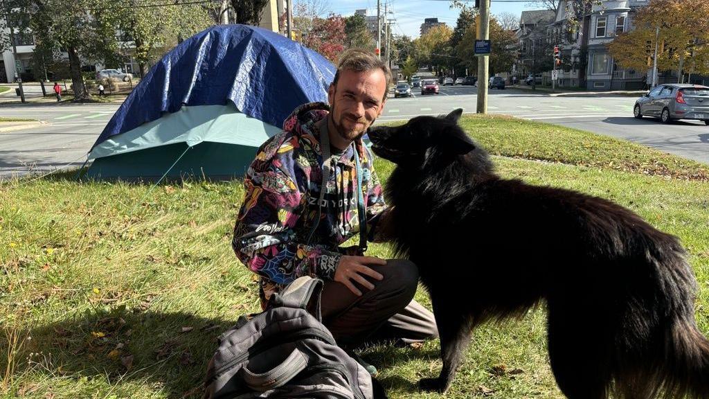 Andrew Goodsell poses outside his tent with his dog in downtown Halifax