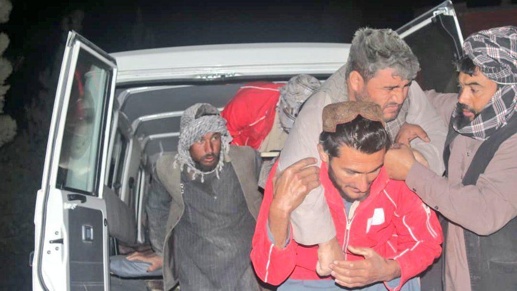 A man in red jacket carrying an older man out of a truck on his back. Other people stand around them trying to help.