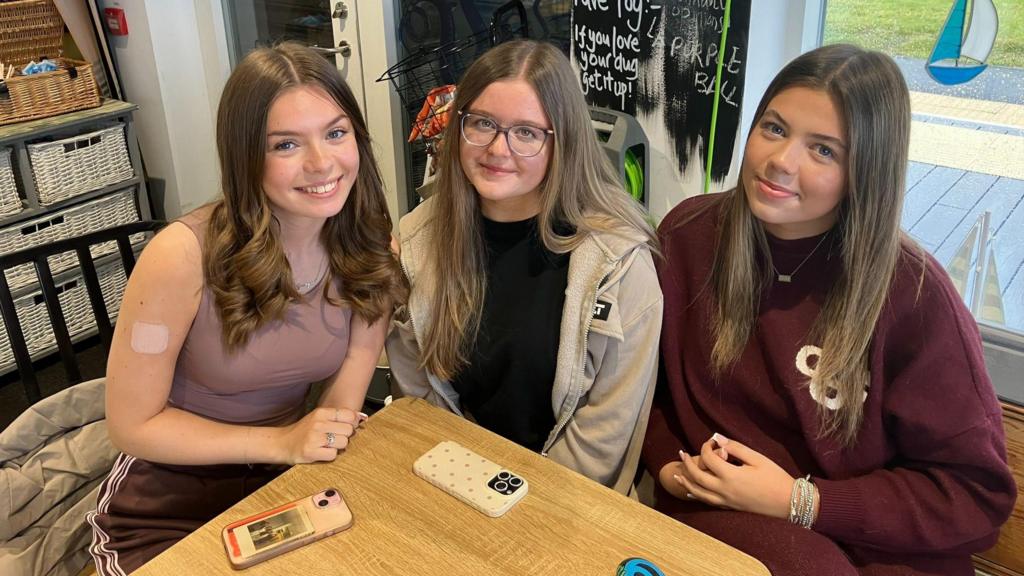 Three female students in a cafe with their phones on a table in front of them