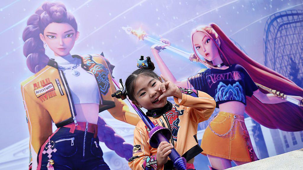 as little girl dressed as Rumi from Kpop demon hunters poses in front of a big poster of Rumi and Mira