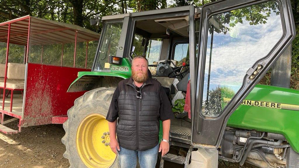 Peter Plummer, a bearded man in a functional gilet, stands next to a tractor