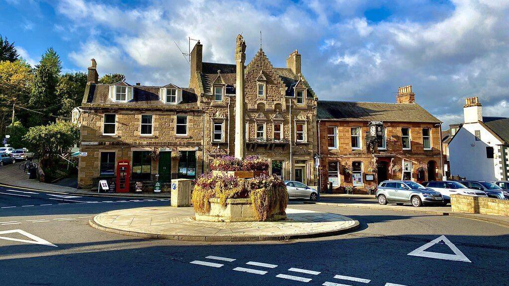 Melrose Market Square - a large three storey sandstone building behind a roundabout, in the centre of which is a monument.