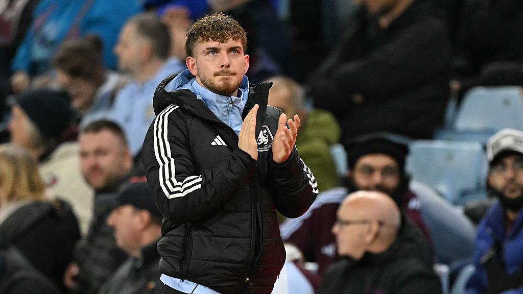 Harvey Elliott applauding while wearing an Aston Villa coat