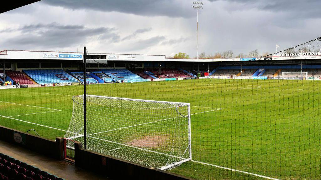 A view of the pitch at Glanford Park football stadium from behind a goal. The grass is surrounded by blue and claret-coloured seats. A floodlight can be seen at one end of the ground.