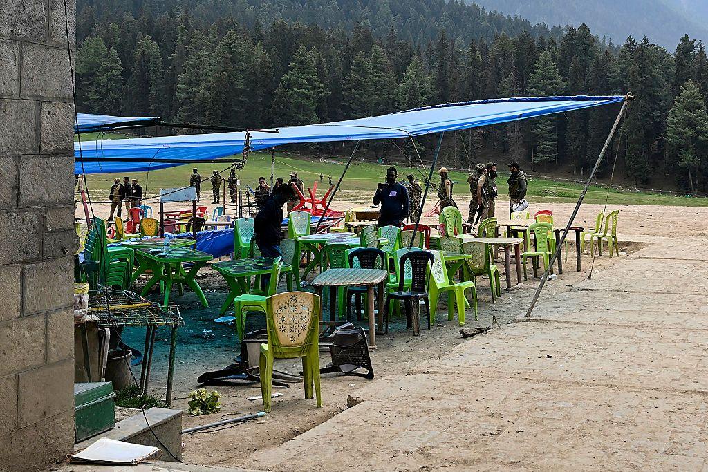 Security personnel inspect the site in the aftermath of an attack as green, plastic food stall chairs lie under a sheet of tarpaulin in Pahalgam