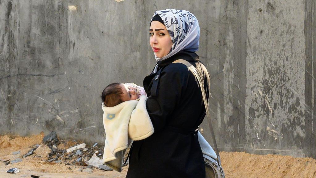  A woman walks down the street holding a baby