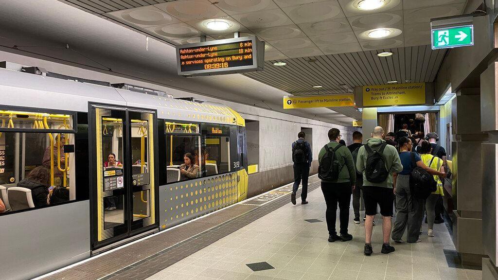 Commuters crowd the bottom of an escalator at the end of a tram metro station at Manchester Piccadilly 