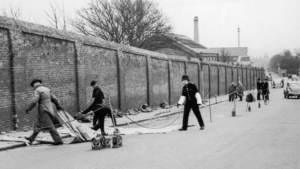 A black-and-white image of police moving items on a street.