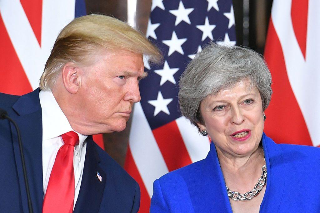 Donald Trump, in red tie and navy suit, leans towards Theresa May, in bright blue blazer, during his 2019 state visit to the UK. Behind them are UK and US flags