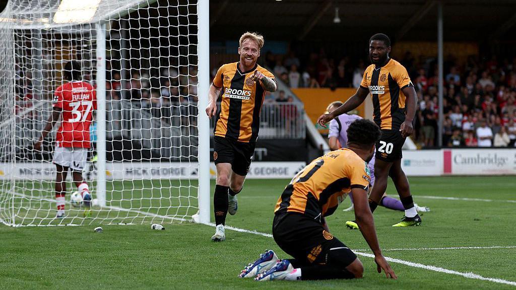 James Brophy runs away smiling and pointing at Elias Kachunga, who set up his opening goal for Cambridge United against Charlton Athletic