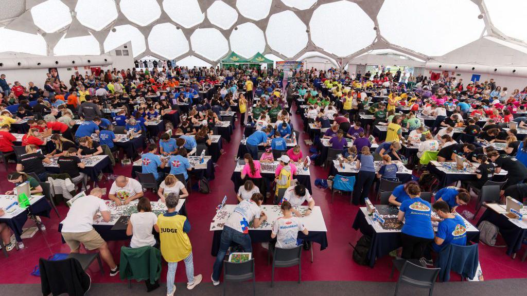 A hall with lots of tables in it where people are trying trying to piece together jigsaws