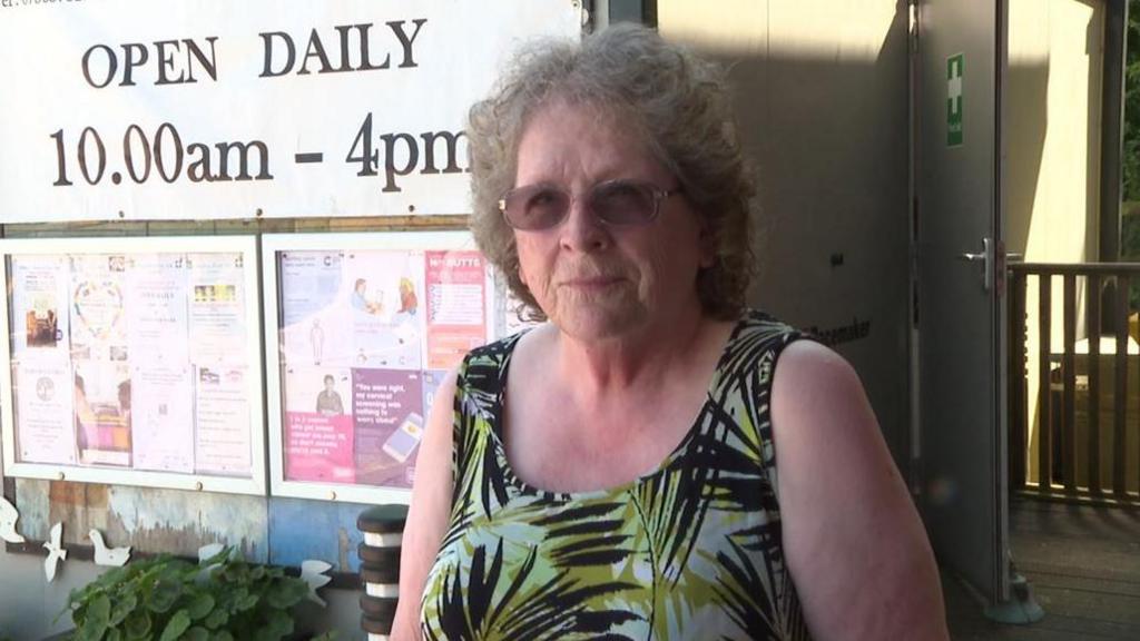 Trustee and chair Rosie Bullard, wearing a black, green and white floral dress, standing in front of the centre