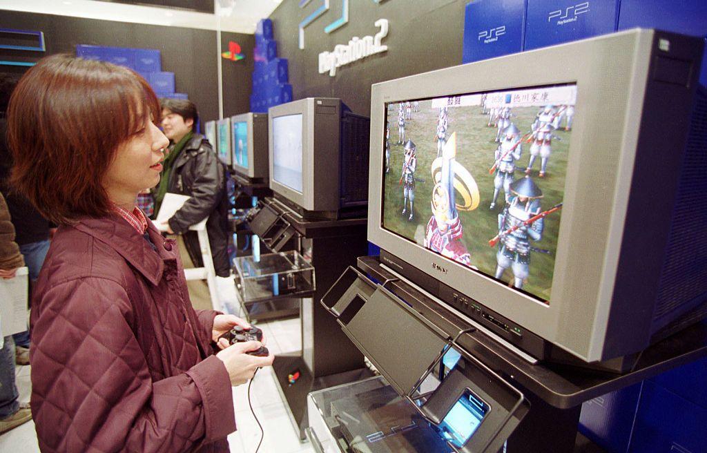 Image shows a woman playing a PS2 on a TV screen in a shop. 