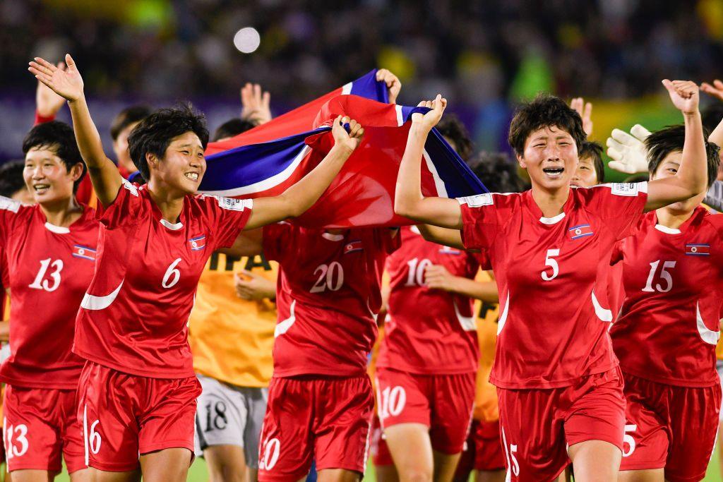 Half a dozen North Korean players jubilantly run and cheer, while waving their country's flag.