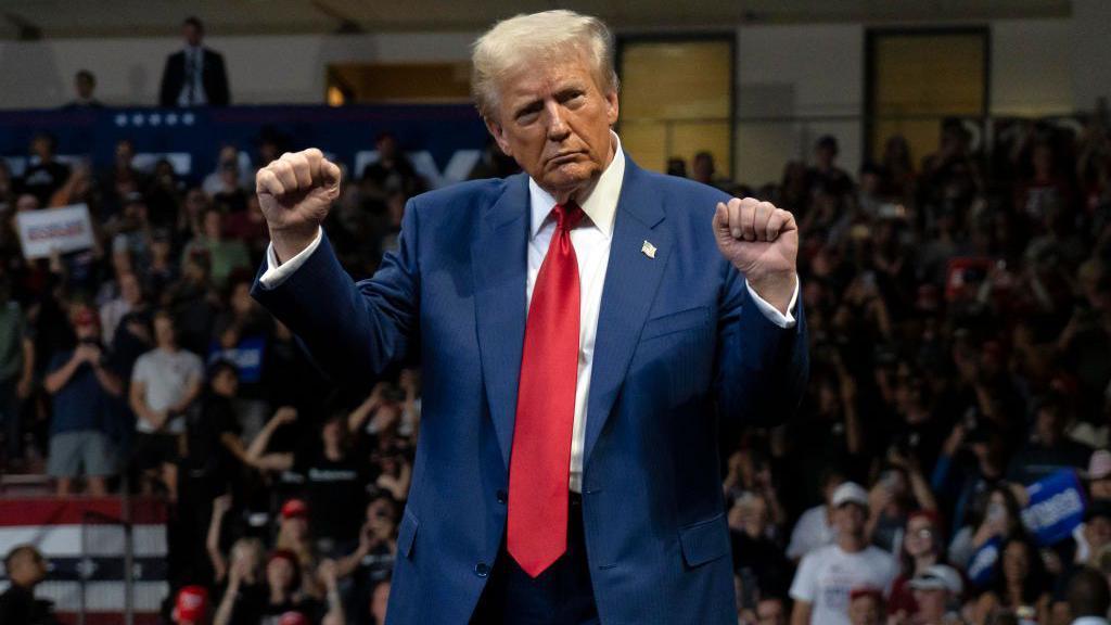 A picture of Donald Trump wearing a red tie dancing at a campaign rally. 