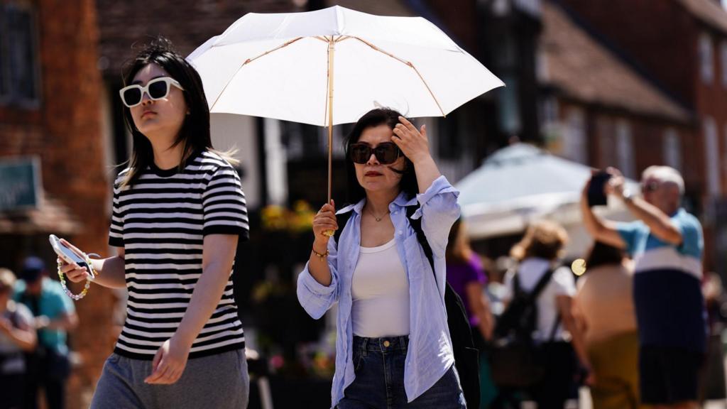 A woman holds an umbrella in Stratford-upon-Avon in Warwickshire. The UK is set to bake in record-breaking temperatures which could soar to more than 38C as the Met Office has issued a rare red weather warning for extreme heat in central and southern England and Wales on Wednesday and Thursday