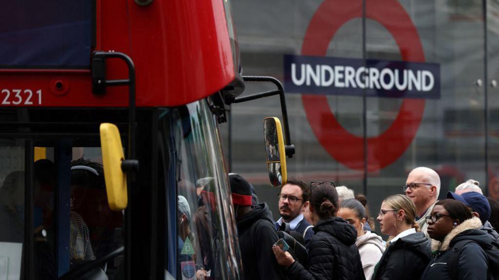 File image showing commuters attempting to board a red London bus outside Victoria train station in London in 2022, with the underground roundel visible in the background