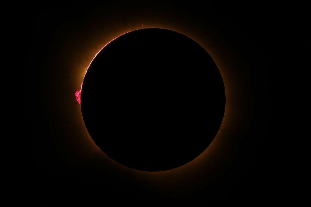 A black darkened sky with a circle of orange light bordering a black circle – the blocked Sun - and small loops of pink can be seen coming from the surface of the Sun
