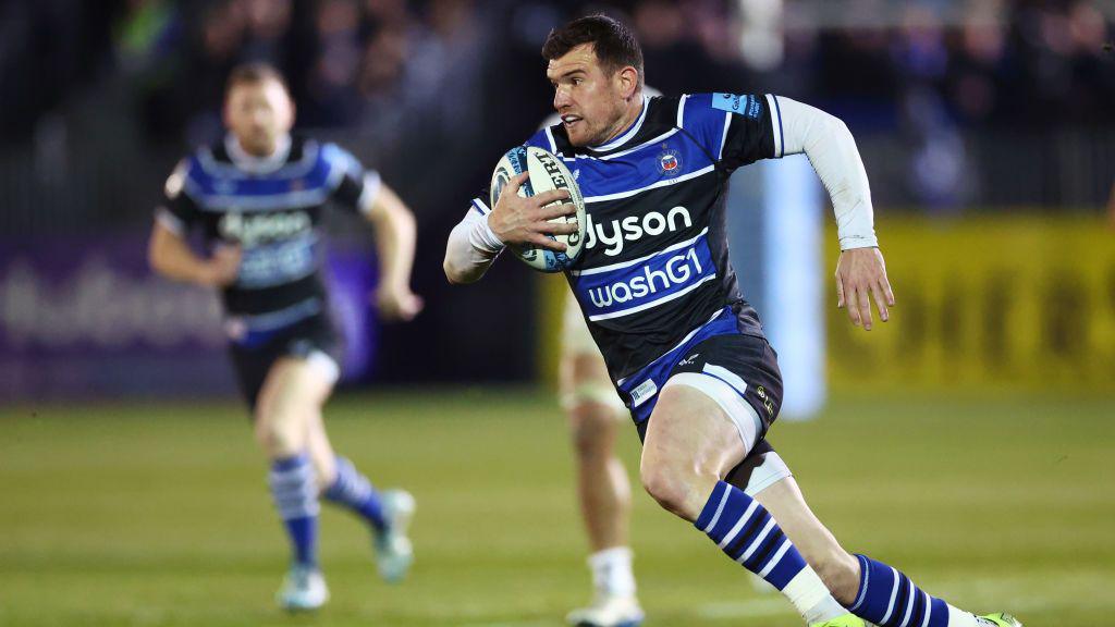 rugby player wearing blue, black and white running with rugby ball in space