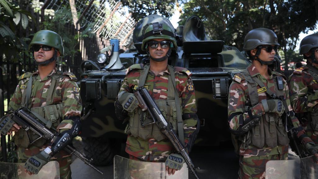 Soldiers in full battle gear, rifles pointed to the ground and carrying shields