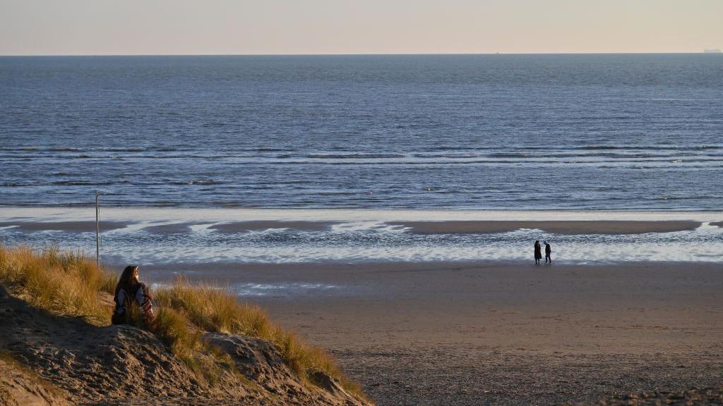 A woman sitting on a sandy beach.