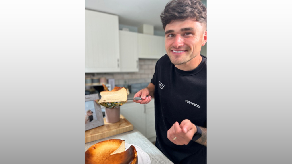 Matty Edgell smiling at the camera as he holds up a slice of cake balanced on a knife