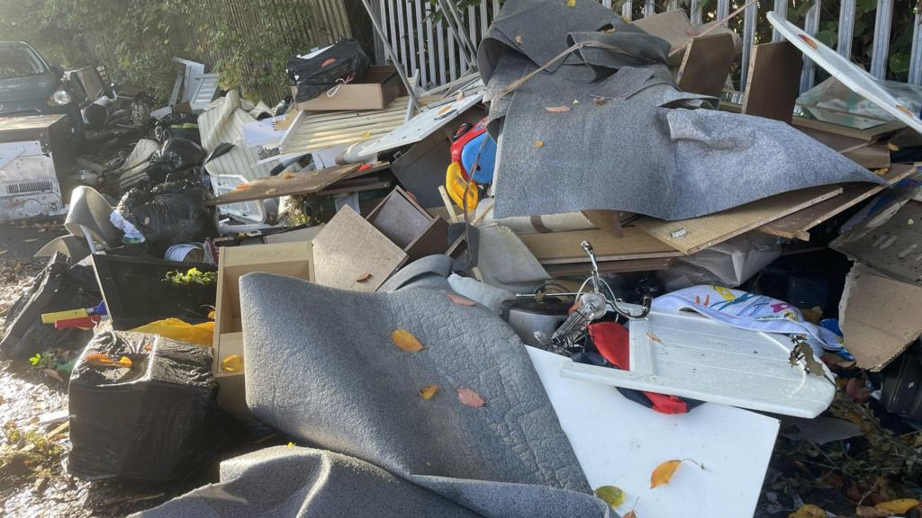A large pile of fly-tipped rubbish, including bin bags, bits of carpet and broken furniture