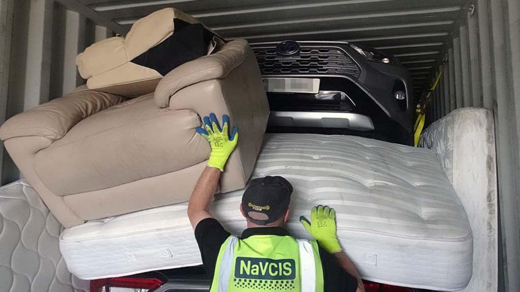 An officer standing in front of a open container with mattresses and a car inside 