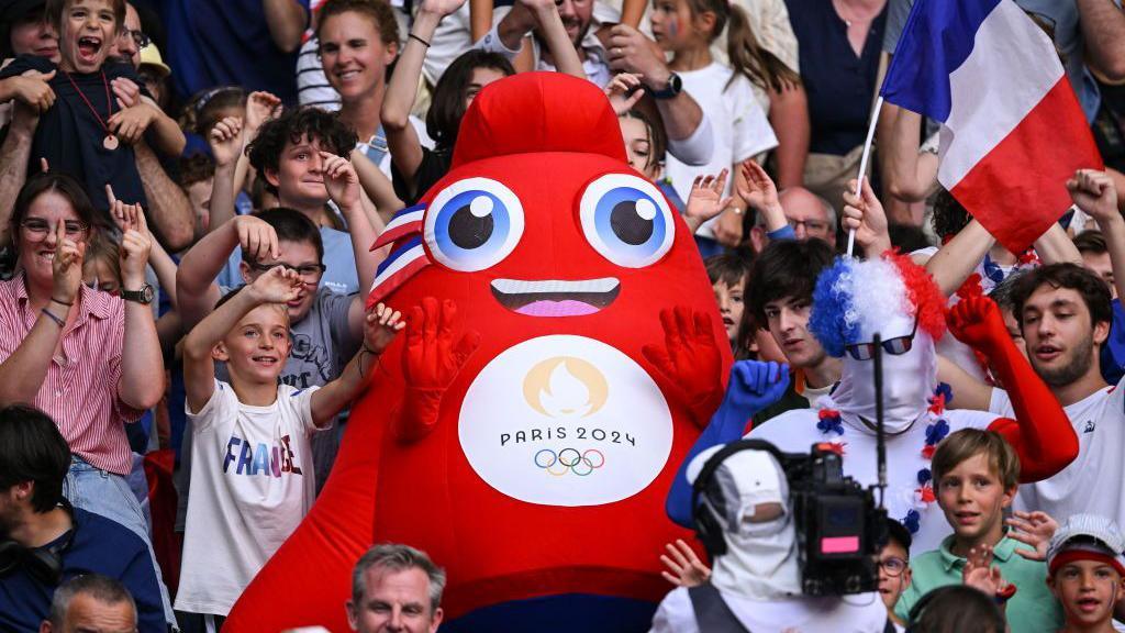 The Paris 2024 Olympic mascot cheering with fans