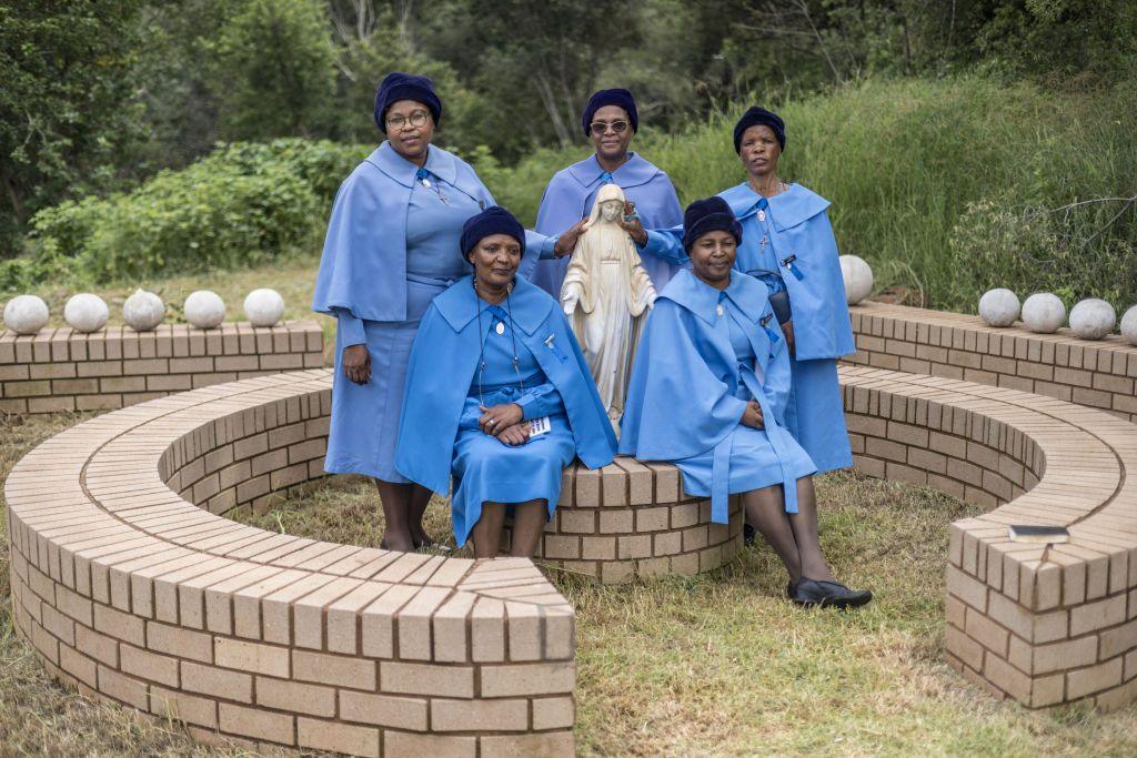 Women dressed in matching blue clothing stand close to a stone statue.