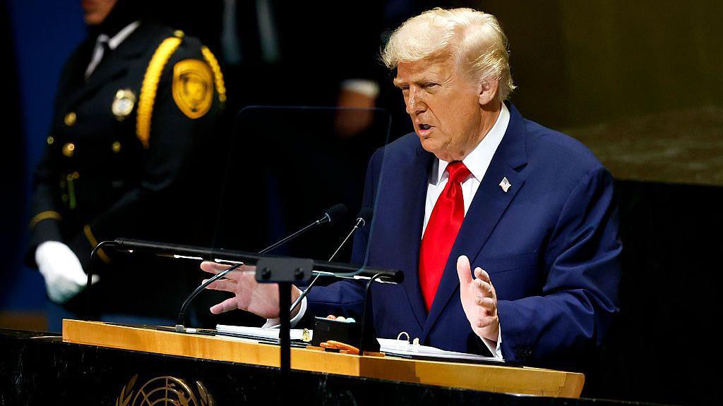 President Donald Trump wearing a blue jacket and red tie gestures with his hands as he stands at a lectern during the 80th session of the UN’s General Assembly (UNGA) at the United Nations headquarters on September 23, 2025 