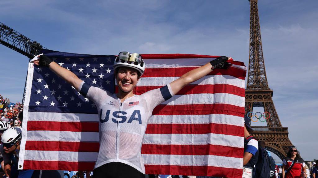 Kristen Faulkner holds up the US flag in front of the Eiffel Tower