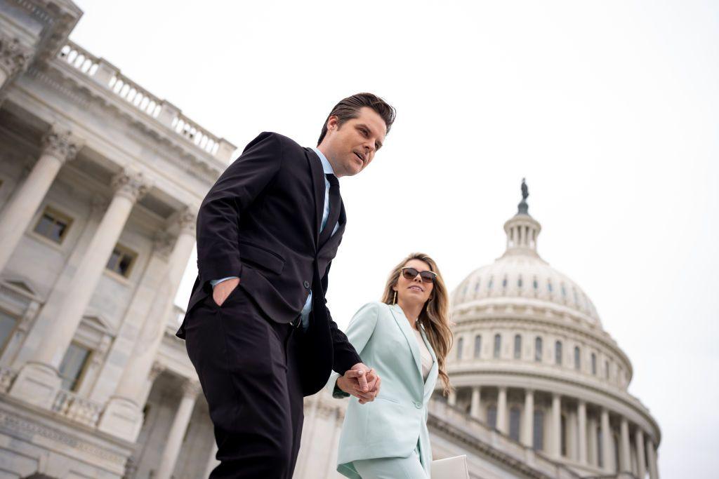 Matt Gaetz and his wife Ginger Gaetz walk down the steps of the House of Representatives in Washington DC. The two are holding hands, with Matt Gaetz in a dark suit and Ginger Gaetz in a mint suit.