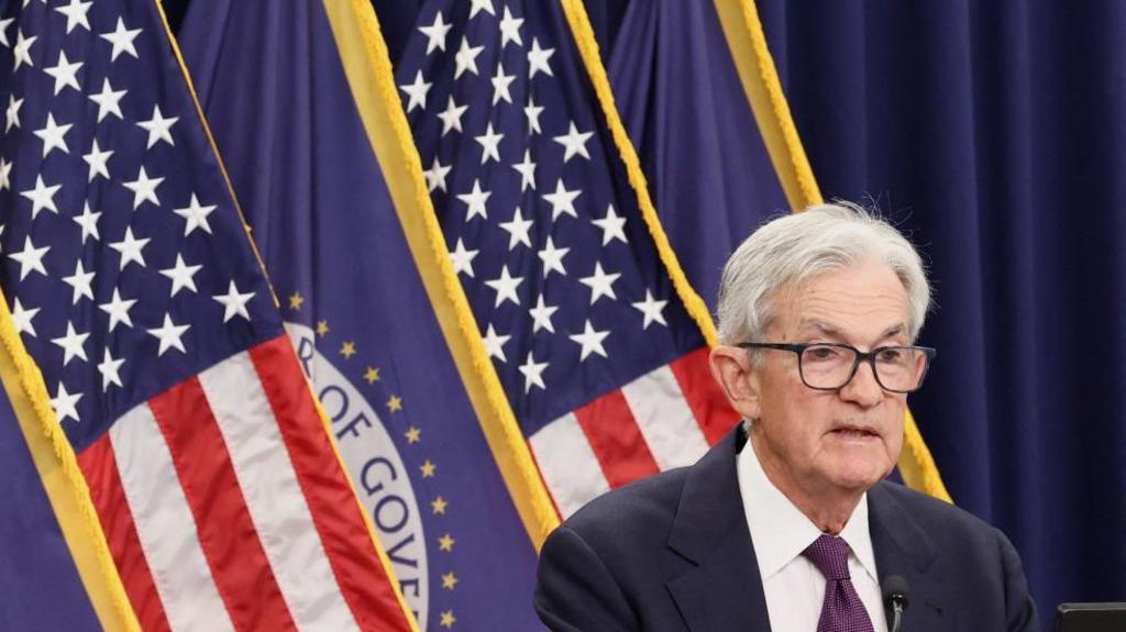 Jerome Powell stands at a lectern in front of a display of flags