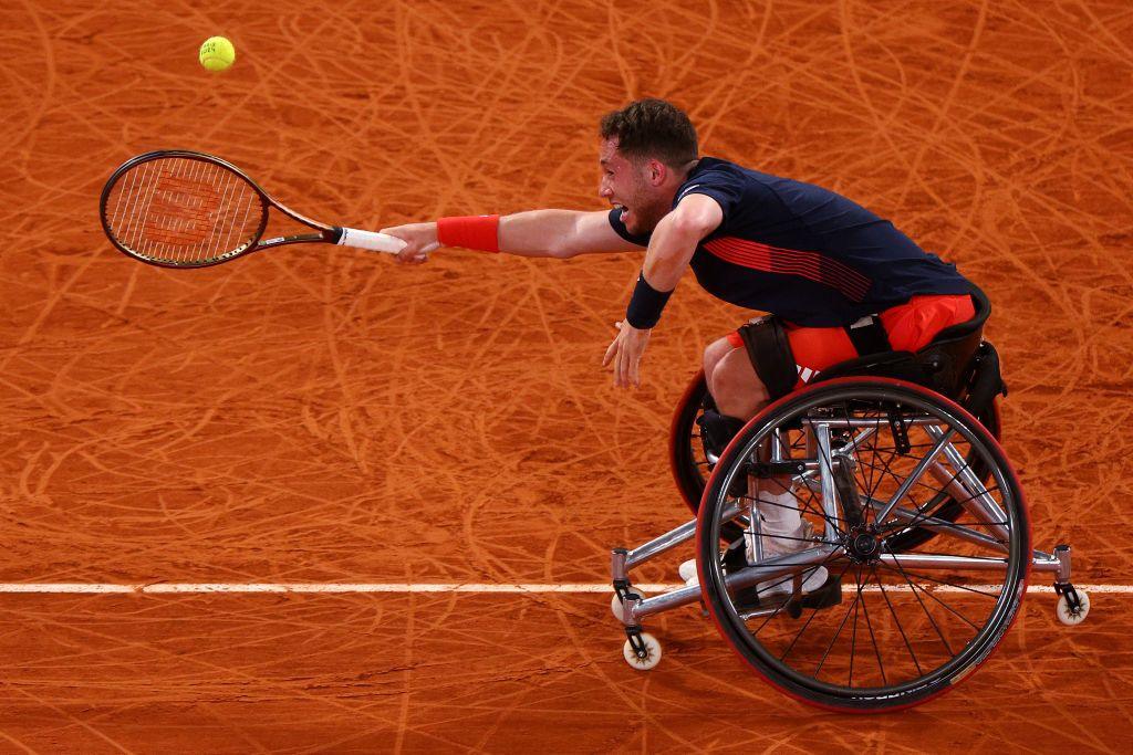 alfie hewett lurches forward in his wheelchair trying to reach a tennis ball on a sand court