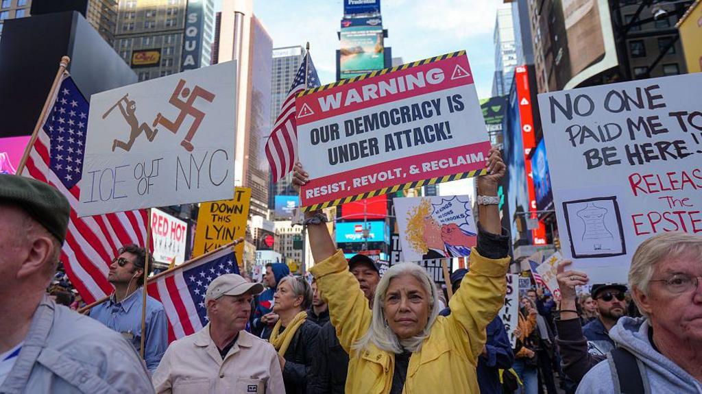 Në Times Square, një grua mban një pankartë ku shkruhej "demokracia jonë është nën sulm".