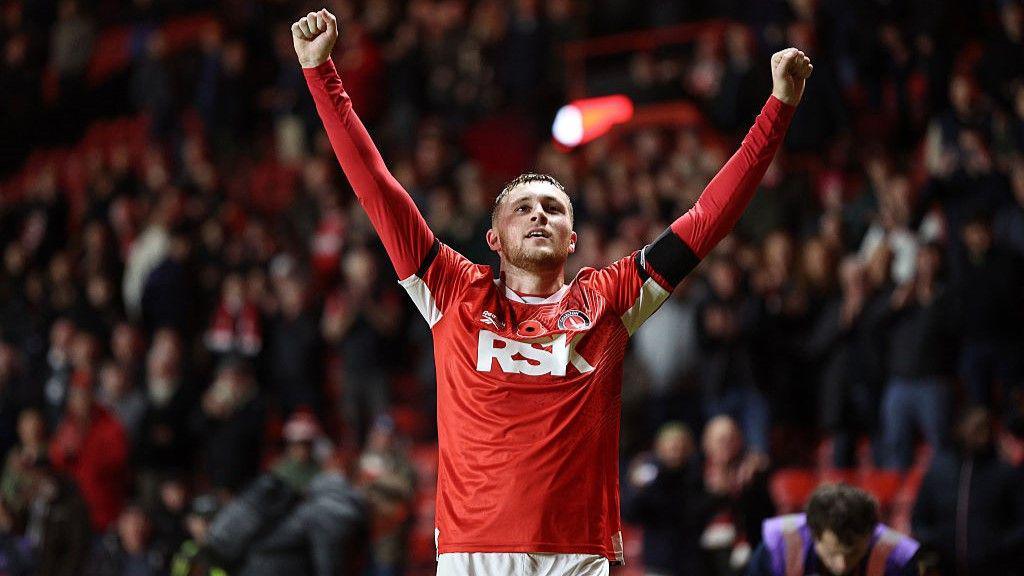Sonny Carey holds arms outstretched in red home kit after scoring late winner
