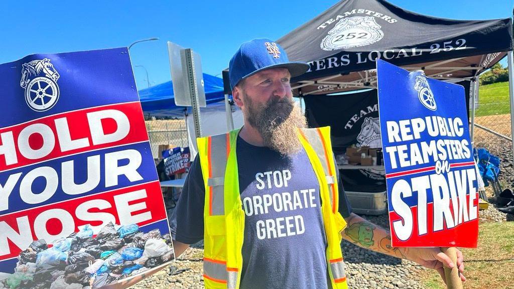 Sanitation worker Will Zekas holds signs reading 'hold your nose' and 'republic teamsters on strike' on the picket line in Washington state