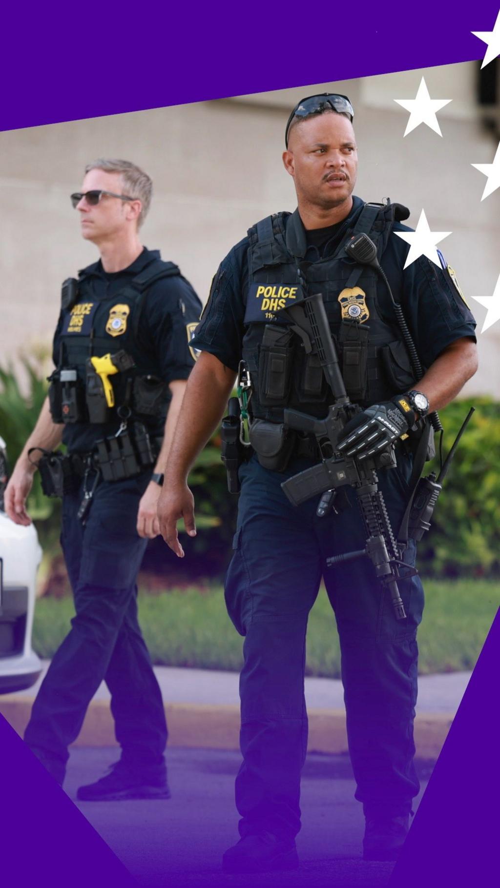 An armed policeman stands in front of a police car