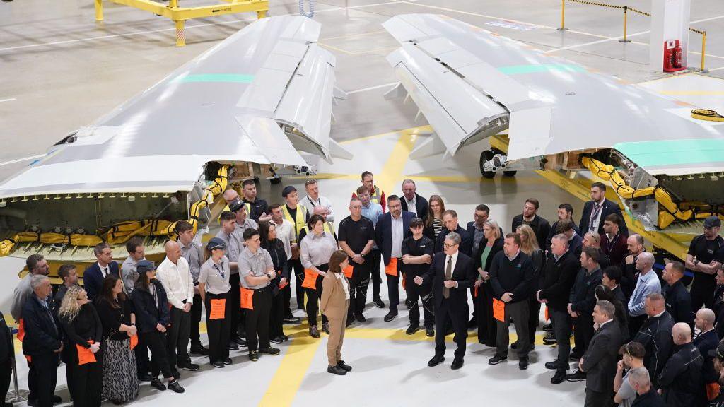 Llun o Brif Weinidog Cymru, Eluned Morgan a Phrif Weinidog y DU, Syr Kier Starmer yn sefyll o flaen adennydd awyren yn ystod ymweliad â chwmni awyrofod Airbus. Mae llwyth o aelodau staff wedi eu hamgylchynnu.