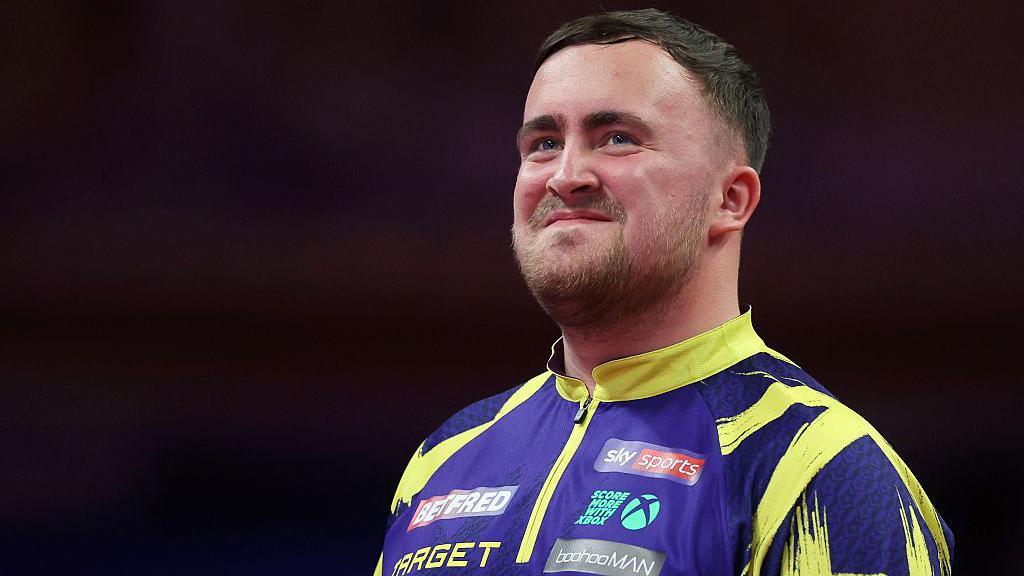 Luke Littler smiling wearing his darts kit