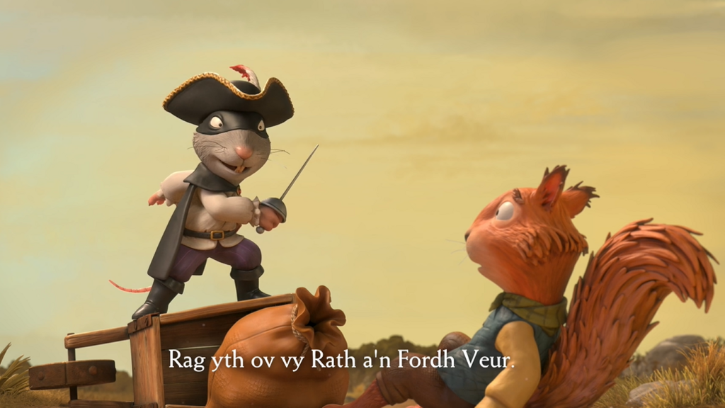 Image taken from Highway Rat animation showing the title character - a rat dressed as a highway robber - brandishing a sword while standing on a upturned wheelbarrow with a sack next to it and a squirrel edging away having fallen to the floor with subtitles in Cornish.
